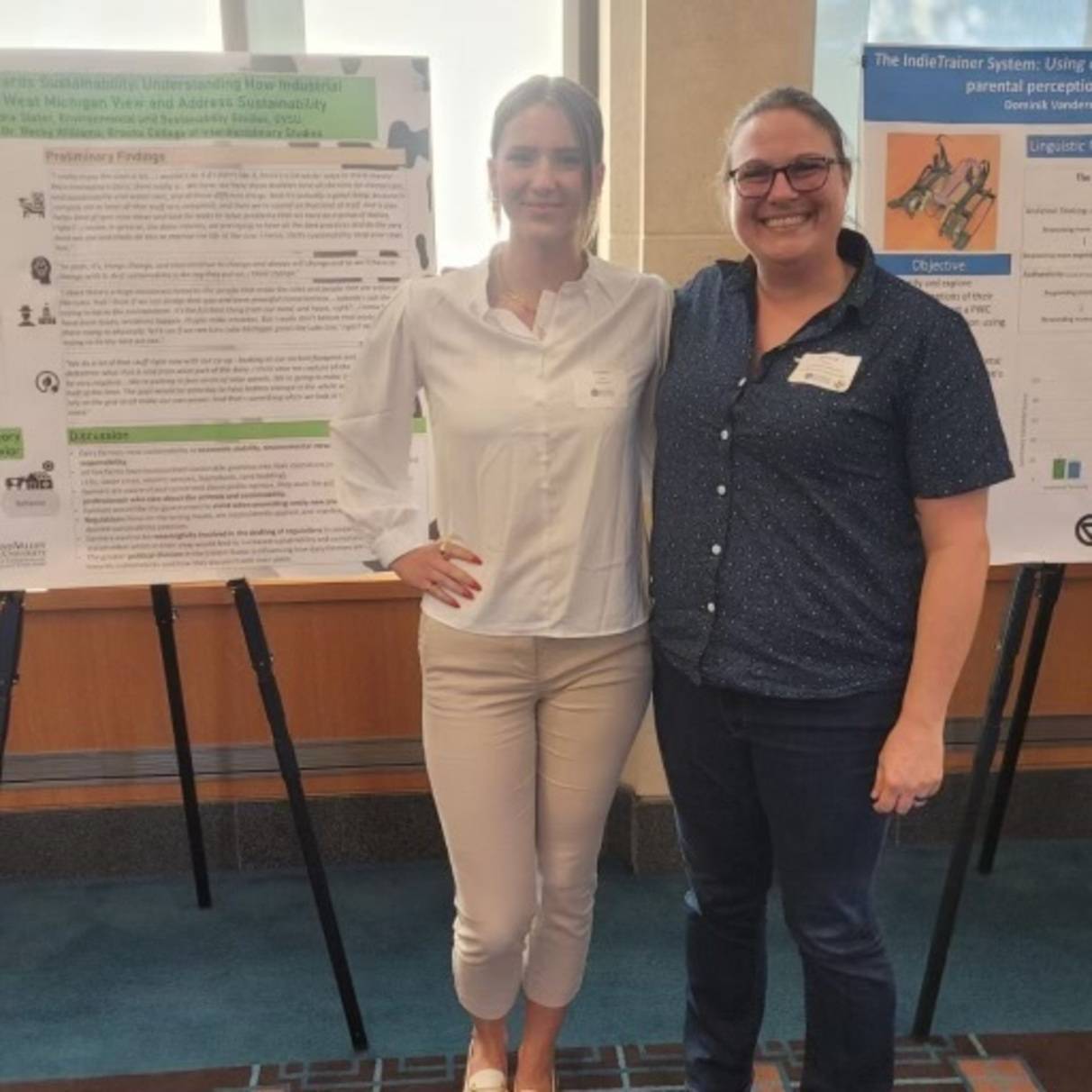 two people standing in front of a poster display smiling for the picture